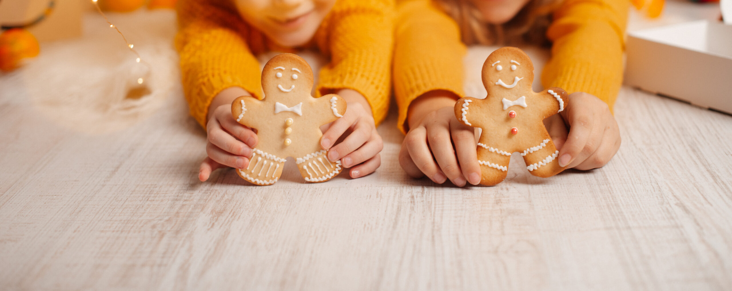 Zwei Kinder im gelben Pullover halten dekorierte Lebkuchenmännchen in den Händen.